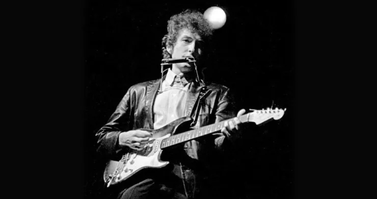 Black and white photo of a musician playing an electric guitar and harmonica on stage.