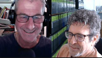 Two men smiling and engaging in conversation during a video call, with bookshelves and filing cabinets visible in the background.